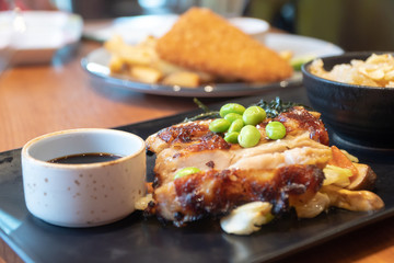 close up of chicken steaks with cup of sauce on the black plate. Green peas and Japanese seaweed on chicken steaks with white cabbage, carrots and mushrooms in the restaurant