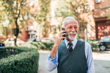 Modern senior business man talking over mobile phone outdoors.