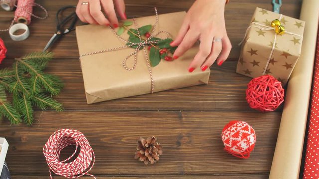 High angle view of Christmas gift box wrapped in craft paper and tied with plain baker's twine on the dark wooden planks with decorating elements Holidays and Gifts concept.