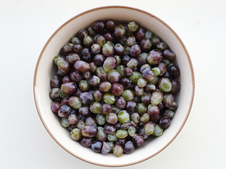 A white ceramic bowl containing red and green wet grapes without the stalks, on a white surface