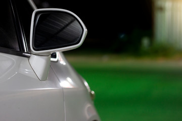Fototapeta na wymiar Side view mirror of white car parking facing the street at night.