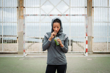 Urban latin sporty woman taking a rest for drinking nutritive detox smoothie. Fitness nutrition and outdoor workout concept.