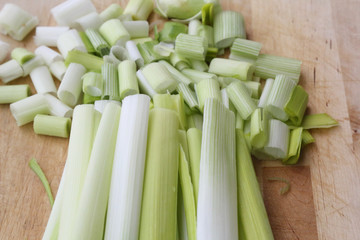 A bunch of clean, fresh and wet leek vegetables, already detached and ready to be cut, minced and sliced, on a light wooden board on a white surface