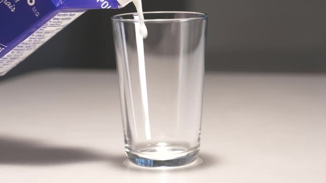 Milk is poured into a glass.  The glass is then picked up. Shot in high speed photography.
