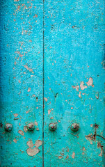 Vertical closeup of section of old blue Zanzibar door, Stone Town, Zanzibar, Tanzania.  Paint is cracked and peeling and brass door studs are showing signs of corrosion. Timber is teak or mahogany.
