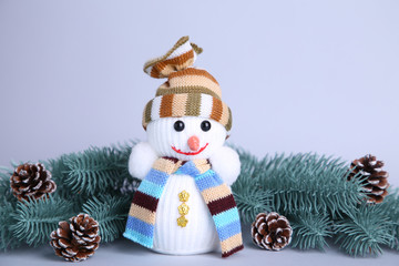 Small snowman toy on a grey background wuth fir-tree branch