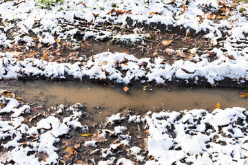 puddle in track of dirty road covered with snow