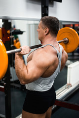 muscular man trains his shoulders with a barbell in the gym. Health and fitness concept