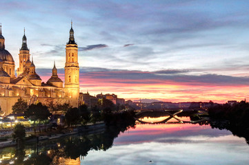 A landscape of Pilar Cathedral and Santiago Bridge reflecting in the Ebro river at sunset, after a storm, in a cloudy autumn, in Zaragoza, Spain