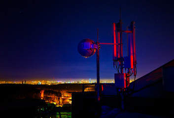 Telecommunications tower, antenna and satellite dish and city at night as background