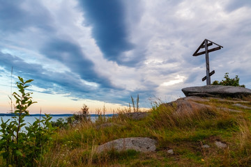 Cross on the rocks of the shore of the lake, the sunset, the ominous clouds