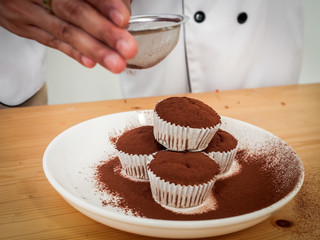 Chef's hand sprinkle chocolate powder on cupcake.