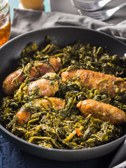 Italian sausages with rapini broccoli in a skillet with table setting on green wooden table