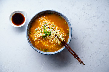 Top view picture of easy japanese ramen with noodles, pork broth, egg and leek in handmade blue ceramic bowl with wooden chopsticks. Concrete background, copy space