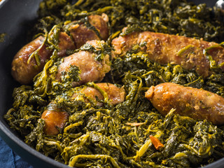 Italian sausages with rapini broccoli in a skillet with table setting on green wooden table