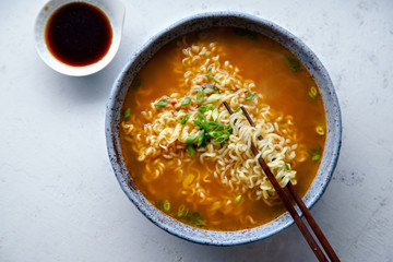 Top view picture of easy japanese ramen with noodles, pork broth, egg and leek in handmade blue ceramic bowl with wooden chopsticks. Concrete background