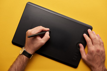 cropped shot of man drawing with graphics tablet on yellow surface
