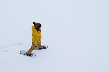 Fototapeta na wymiar man in a yellow jacket walking in the snow in snowshoes