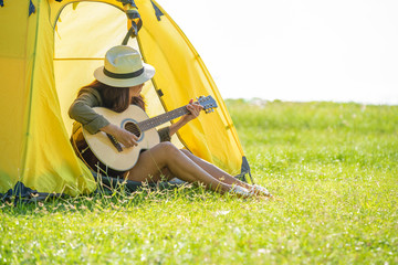 Beautiful women camping and playing a guitar surround with fresh air on sunny day. Women having a holiday alone in countryside.