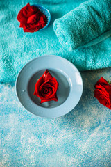 The concept of Spa and self-care: rose water with red rose flowers, next to a towel on a blue background.