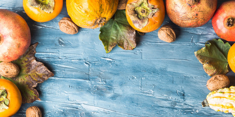 Autumn fruit thanksgiving background with persimmons, pomegranate, apples, nuts, squash on blue...