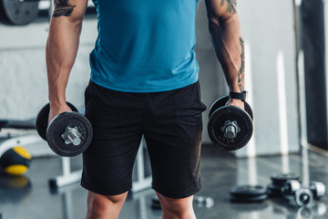 midsection of young sportsman exercising with dumbbells in gym