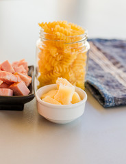 Pasta in jar with cheese and baked ham pieces in bowls isolated on white background, close-up