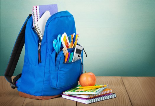 Colorful school supplies in backpack on blackboard background