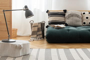 Scandinavian futon with patterned pillows in natural interior with white wall and parquet on the floor, real photo