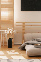 Hygge inspired bedroom with scandinavian futon as a bed and white flowers in black vase, real photo...