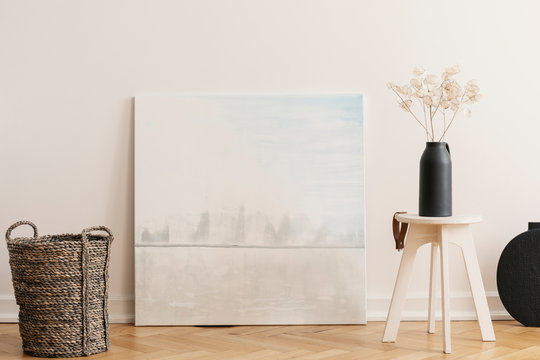 Abstract painting between wicker basket and wooden table with black vase with flowers, real photo with mockup