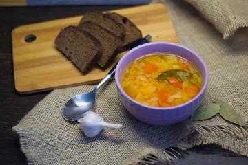 A plate of cabbage soup and potatoes on a wooden table, next to the black pieces of bread.
