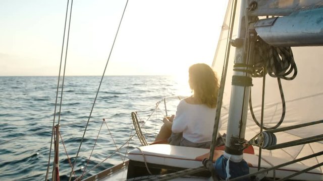 Young girl in a dress sits on the deck of a sailing yacht near the mast
