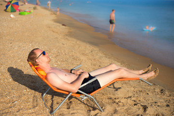 a young guy in sunglasses lying on a sun lounger on the beach 