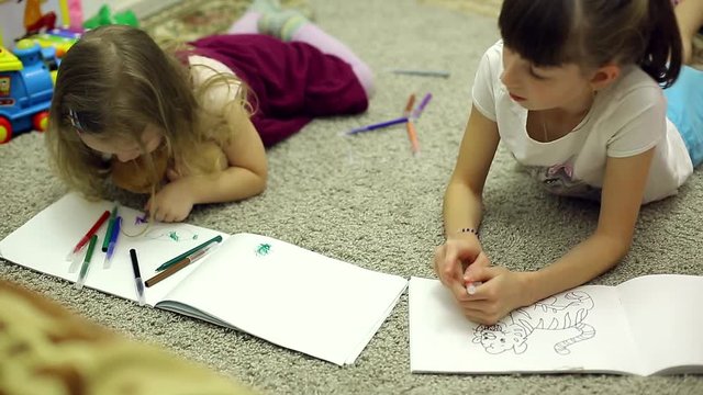 girls draw markers in the album lying on the floor in the room
