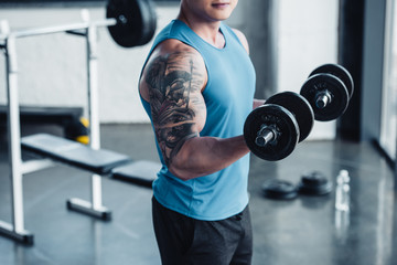 Partial view of young sportsman exercising with dumbbells in gym