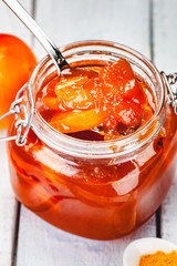 Persimmon jam in glass jar on wooden  background. Close up