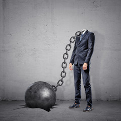 A businessman with a chain connected to a wrecking ball instead of his head stands on a concrete...