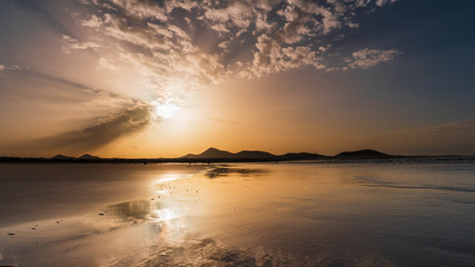 Obraz premium Empty beach at sunset with mountain silhouettes in the distance. Famara Beach, Lanzarote, Spain.