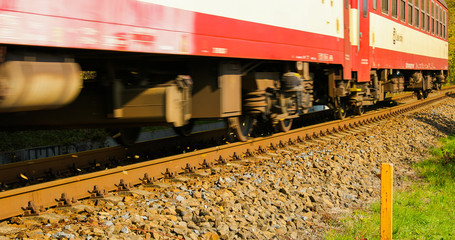 A detailed view of a train passage with two wagons captured in slow motion during a sunny day from the track then moves the leaves after the passage.