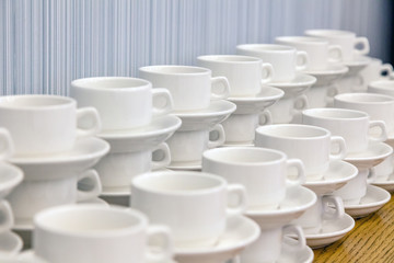 Fototapeta na wymiar Lot of white porcelain tea pairs in piles in a straight line. Concept conference at the hotel, break, catering, breakfast