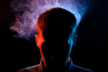The man's face is hidden in the shadows on a black isolated background with red and blue smoke from...
