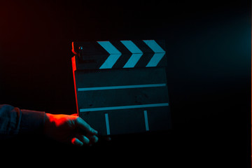 Closed clapperboard for cinema in hand, before filming on a black isolated background with red and...