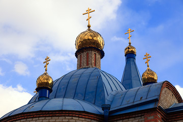 Fototapeta na wymiar Old Christian church in Kemerovo with golden and gilded domes and blue iron roof against a sky. Concept faith in god, orthodoxy, prayer
