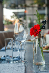 Transparent glass vase with colourful bouquet of flowers against background of table setting in restaurant. Wine and water glasses stand in a row on wooden table. Concept banquet, birthday, conference