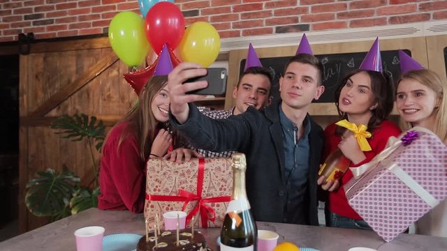 Cheerful friends taking selfie at the birthday party, good-looking young people celebrating important event after work in spacious flat