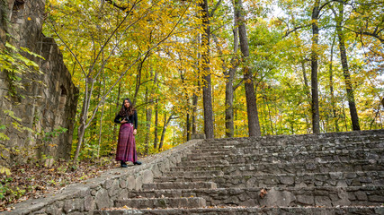 Woman in sarong standing on side wall in stone amphitheater in with yellow leaves behind