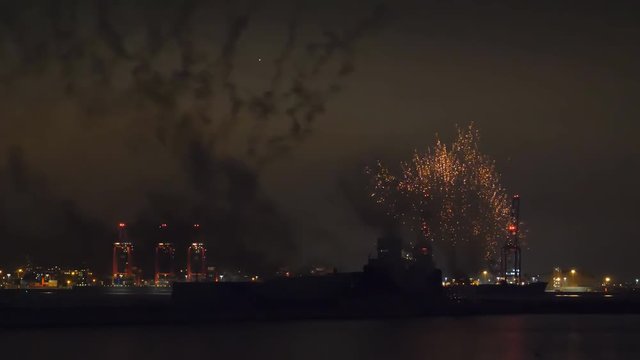Bush like fireworks being shot from Fort Perch Rock in Liverpool Bay with Bootle docks cranes lights seen across river Mersey in the background at night 