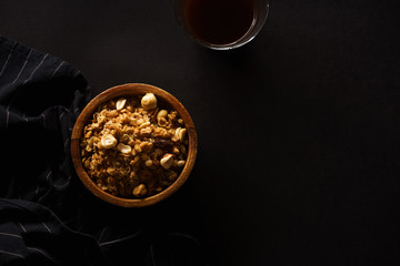 Roasted granola with nuts in wooden bowl with a cup of coffee on black table.