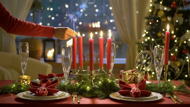 Fale hand lights christmas candles. Festival red table setting with garland and Christmas tree in the background Slow motion